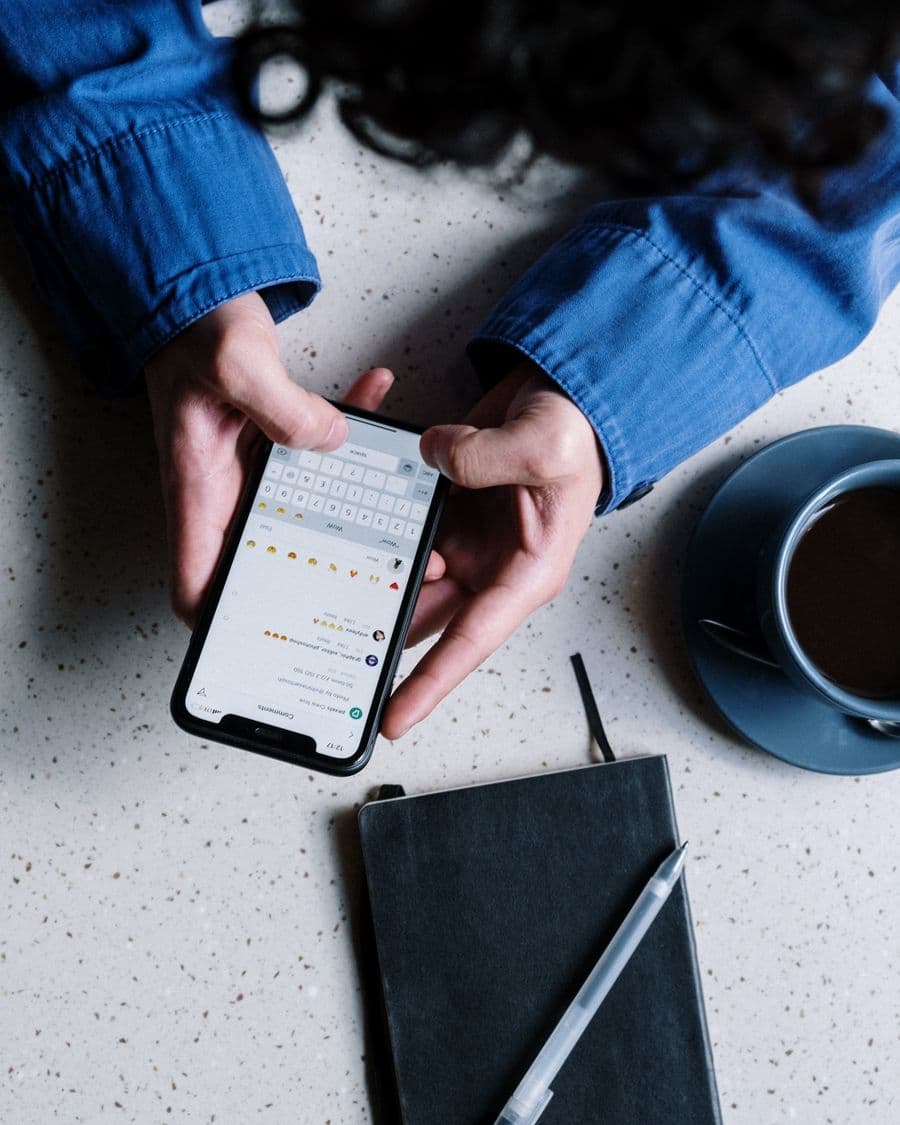 Hands typing a message on a phone beside a coffee cup in daylight
